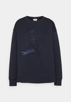 Sudadera azul marino con un diseño de escudo bordado en relieve con laureles y una bandera con la inscripción "TOMMY HILFIGER." Manga larga, cuello redondo.