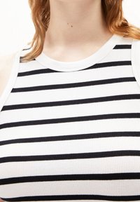 Närbild av en person som bär en vit ribbad ärmlös topp med horisontella svarta ränder, som visar hals och övre bröst.