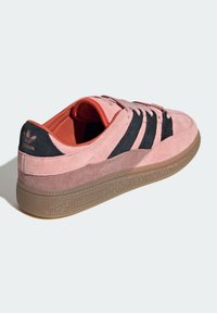 Suede sneakers in pink and black, featuring three black stripes, rubber sole, and woven laces. Textured upper with contrasting inner lining.