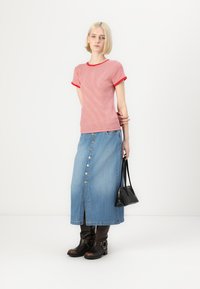 Rød og hvit stripete t-skjorte med rød kant, paret med en blå denimskjørt med frontknapper og splitt, båret med brune støvler.