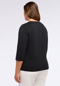 Top negro de manga larga con escote redondo y textura suave. Lleva puesto sobre pantalones de color claro, mostrando un diseño sencillo y limpio.