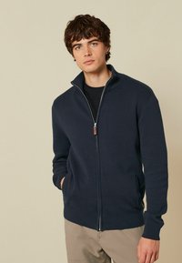 Marinefarbener Reißverschluss-Pullover mit Stehkragen, gerippten B�ündchen und Saum; beinhaltet zwei Seitentaschen und einen ledernen Reißverschluss-Zug.