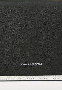 Portafoglio in pelle nera con una finitura testurizzata, dotato di una striscia bianca e logo "KARL LAGERFELD" in bianco in rilievo.