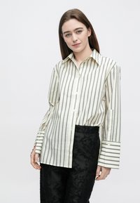 Camisa de botão de manga comprida em creme com riscas verticais pretas. Possui gola pontiaguda e punhos largos com riscas. Textura suave.