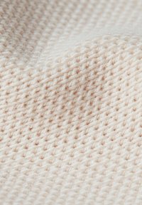 Tessuto a maglia beige chiaro con una trama texturizzata, che mostra una superficie morbida e leggermente pelosa. In evidenza punti uniformi e una caduta delicata.