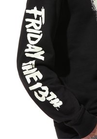 Sudadera negra con "VIERNES 13" en texto blanco desgastado y en negrita a lo largo de la manga; textura suave y ajuste estándar.