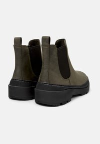 Botas de piel verde oliva hasta el tobillo con paneles laterales elásticos, puntera redondeada y suela de goma negra. Incluyen tiradores para facilitar su uso.