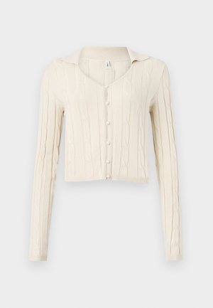 Cream-colored cable knit cardigan with long sleeves, a V-neckline, and five pearl buttons down the front. Cropped design.