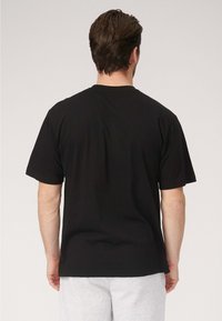 Sort bomulds T-shirt med korte ærmer og rund halsudskæring, set bagfra. Har en afslappet pasform og en glat tekstur.