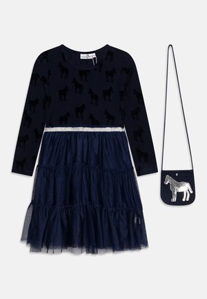 Marineblaues, langärmeliges Kleid mit Pferdemustern oben und gestuftem Tüllrock, kombiniert mit einer kleinen marineblauen Umhängetasche mit silbernem Pferd.