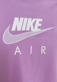 Lila bomull T-shirt med vit broderad "NIKE" logotyp och prickad swoosh-grafik ovanför ordet "AIR". Slät textur.
