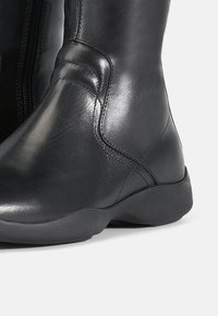 Bota de tornozelo em couro preto com textura suave, biqueira arredondada, costura discreta e sola de borracha baixa para conforto. Fecho com zipper na lateral.