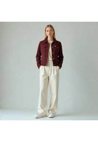 Vinrød ruskindjakke med knappet lukning foran, brystlommer og krave, kombineret med beige bukser med vide ben og hvide sneakers.