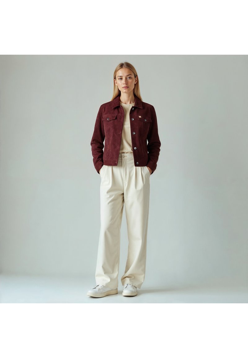 Vinrød ruskindjakke med knappet lukning foran, brystlommer og krave, kombineret med beige bukser med vide ben og hvide sneakers.
