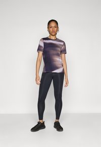 Kortermet, lilla og svart gradient treningsskjorte kombinert med sorte leggings og sorte joggesko. Glatt stoff med en tettsittende design.