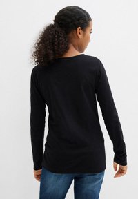 Maglietta nera a maniche lunghe realizzata in un materiale morbido, con scollo rotondo e vestibilità rilassata, abbinata a jeans blu.