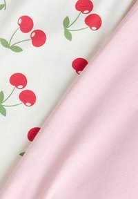 Tissu blanc avec des motifs de cerises rouges à côté d'un tissu rose clair uni, les deux ayant une texture douce et lisse.