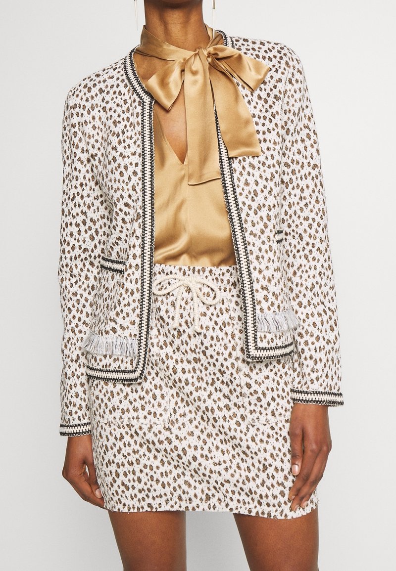 Leopardi-kuosiset bleiseri ja mini-hame setti valkoisena ja ruskeana mustilla yksityiskohdilla. Sisältää silkkisen nauhakiinnitteisen paidan ja fringed yksityiskohdat taskuissa.