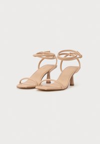 Sandales à talons nues avec un bout ouvert, de fines lanières, une boucle à la cheville et un petit talon bloc. Texture lisse et design minimaliste.