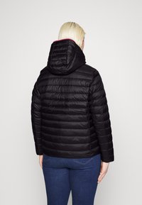 Sort dynejakke med hætte, quiltet design og let skinnende overflade. Har lyserøde detaljer langs kanten af hætten. Set bagfra vises den tætsiddende pasform.