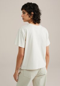 Relaxed-fit, short-sleeve cream t-shirt made of soft cotton. Features a crew neckline and a straight hem. Worn with light beige pants.
