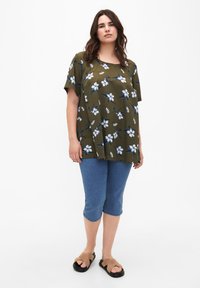 Top floreale verde oliva con fiori blu e bianchi, maniche corte e vestibilità comoda, abbinato a pantaloni capri in denim e sandali marroni.