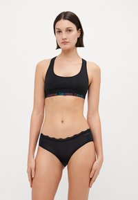 Svart sport-bh med ett flerfärgat Calvin Klein-logoband; matchande svarta underkläder med spetsdetaljer längs midjan. Slät tyg.