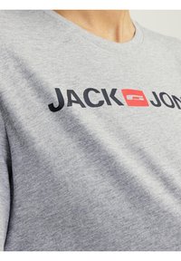 Camiseta de algodón gris con cuello redondo y el texto "JACK" en negro y "JONES" en negro con un acento cuadrado rojo.