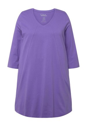 Tunika s výstřihem do V a tříčtvrtečními rukávy v jednofarebné fialové barvě z bavlny. Má volný střih se bočními švy a mírně zakřiveným lemem.