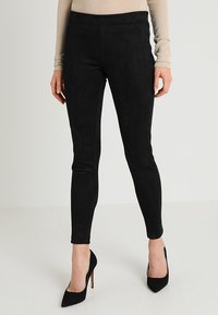 Leggings neri in finta pelle scamosciata con una texture liscia, vestibilità slim e vita alta, abbinati a tacchi a spillo neri.