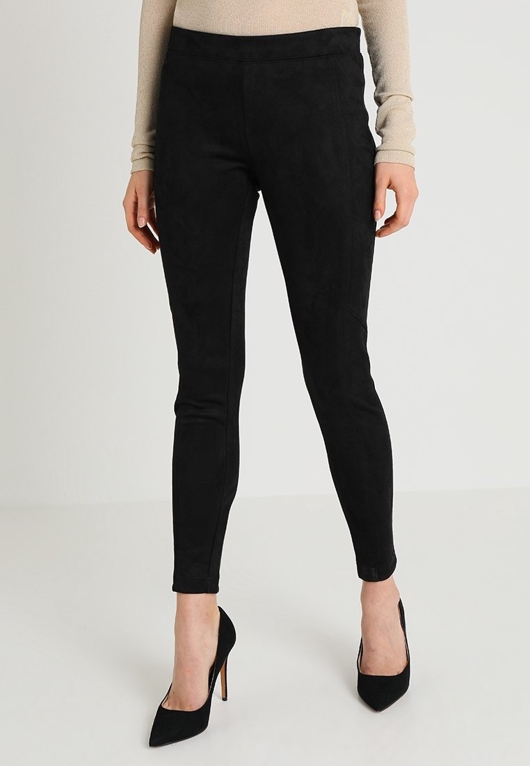 Leggings neri in finta pelle scamosciata con una texture liscia, vestibilità slim e vita alta, abbinati a tacchi a spillo neri.
