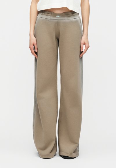 Άτομο που φορά χαλαρά, ταουπέ φόρμες με γκρι ρίγες στο πλάι και λογότυπο "OFF" στη ελαστική μέση, στέκεται μπροστά σε απλό φόντο.