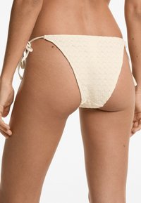 Tejhes szövetből készült, krém színű bikini alsó, mintás dizájnnal és oldalsó megkötőkkel az állítható illeszkedés érdekében.