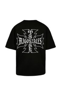Juoda medvilninė trumpomis rankovėmis marškinėliai, ant nugaros centre – didelis baltas kryžiaus grafikas ir tekstas „MIGONZALES“.