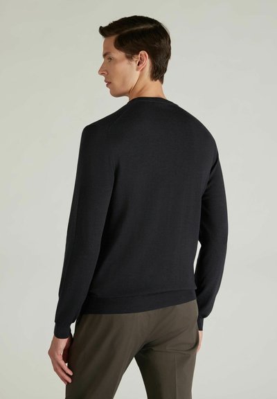 Czarny sweter dzianinowy z okrągłym dekoltem i długimi rękawami, o gładkiej fakturze i ściągaczu u dołu, noszony na oliwkowych spodniach.