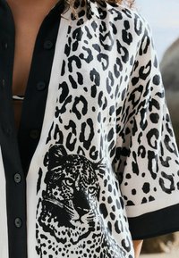 Černobílá košile na knoflíky s designem leopardího potisku a velkým leopardím grafickým motivem. Vyrobena z lehkého materiálu s krátkými rukávy.