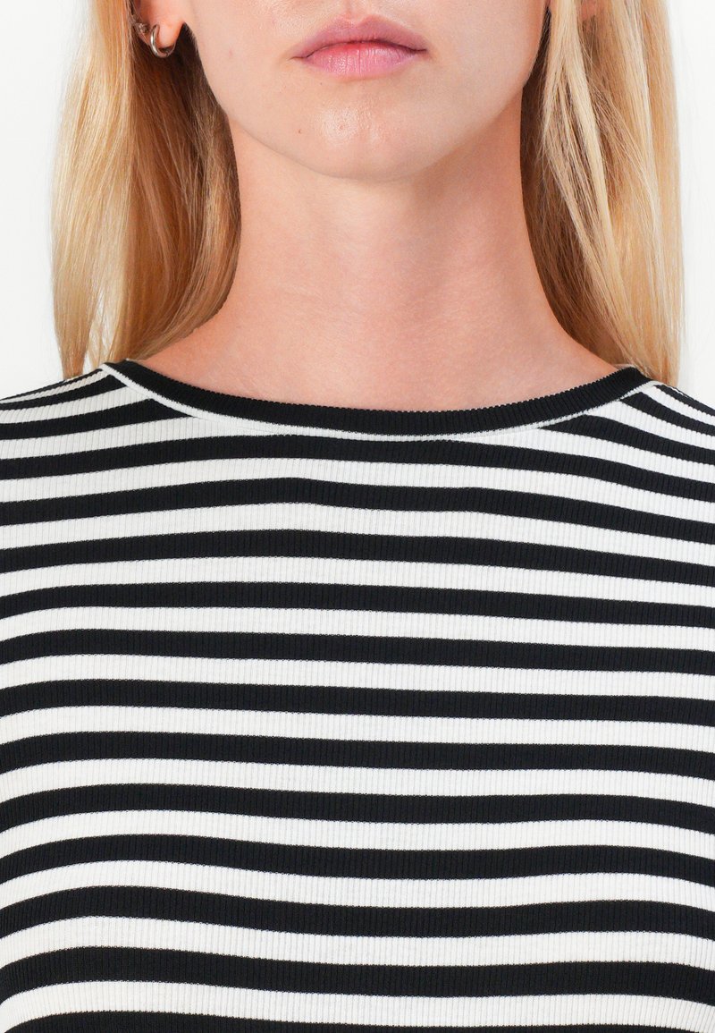 Gestreiftes Top in Schwarz und Weiß mit Rundhalsausschnitt. Rippenstruktur, enganliegendes Design, das den oberen Brustbereich zeigt.