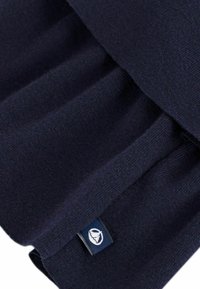 Tessuto a maglia blu scuro con una morbida texture caratterizzato da un design plissettato. Include un piccolo etichetta di marca cucita con un logo.