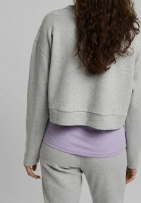 Szary skrócony sweatshirt z długimi rękawami, noszony na lawendowej bluzce z długim rękawem, w połączeniu z dopasowanymi szarymi joggerami o luźnym kroju.