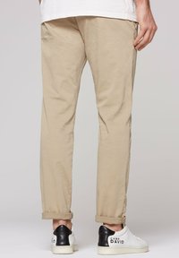 Beige cotton trousers with cuffed hems, paired with white sneakers featuring a black heel accent and "CAMP DAVID" printed detail.