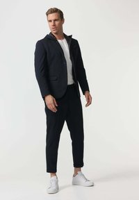 Sacou albastru marin cu glugă, două nasturi și un buzunar pe piept, purtat cu pantaloni albastru marin tapered și adidași albi. Textură netedă pe parcursul întregii ținute.