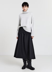 Grauer Strickrollkragensweater mit gerippten Bündchen, kombiniert mit einem schwarzen, knöchellangen, voluminösen Rock. Schwarze kniehohe Stiefel runden das Outfit ab.
