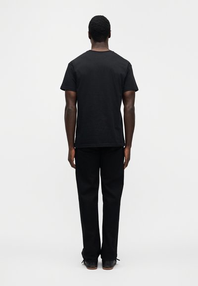 Μαύρο βαμβακερό Τ-shirt με κοντά μανίκια, συνδυασμένο με μαύρο παντελόνι. Η γραμμή είναι άνετη και η υφή φαίνεται λεία.