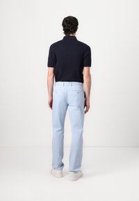 Polo shirt bleu marine à manches courtes avec un design en côtes texturées, associé à un pantalon chino bleu clair. Des baskets blanches complètent la tenue.