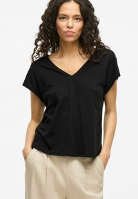 T-shirt nera a V con maniche corte, realizzata in tessuto leggero, abbinata a pantaloni beige chiaro; vestibilità rilassata e texture liscia.