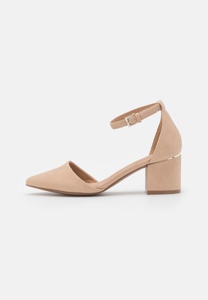 Chaussure beige en daim à bout pointu avec talon bloc, bride cheville et fermeture à boucle, dotée d'un talon bas et solide et de côtés ouverts.
