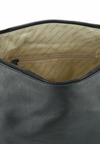 Zwarte leren tas interieur met een gestructureerde afwerking. Ritsluiting en een beige voering met herhaald merklogo. Klein ritsvakje binnenin.