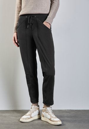 Pantalons de jogging noirs avec taille élastique, poches latérales et coupe fuselée. Associés à des baskets montantes beige et blanches. Texture lisse.