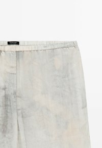 Lichtgrijze, gestructureerde broeken met een elastische tailleband en een subtiel patroon. Merkenlabel "Massimo Dutti" is zichtbaar nabij de bovenkant.