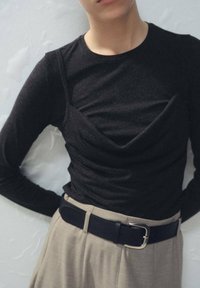 Črn dolg rokav s podrobnostjo z nabranim materialom, kombiniran s bež hlačami z visokim pasom in črnim usnjenim pasom s srebrno zaponko.